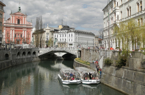Razgled iz mosta na turistični ladjici na Ljubljanici. V ozadju Tromostovje in Prešernov trg.
