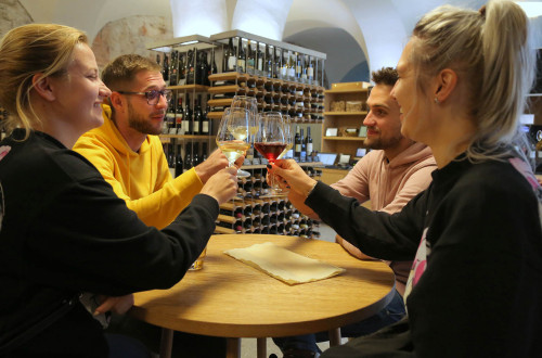 Štirje prijatelji nazdravljajo s kozarcem vina. V ozadju vinska vitrina. 
