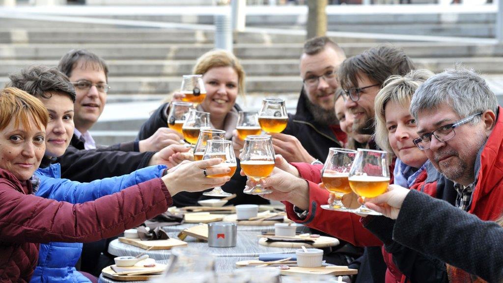 Skupina ljudi za mizo nazdravlja s pivom. 
