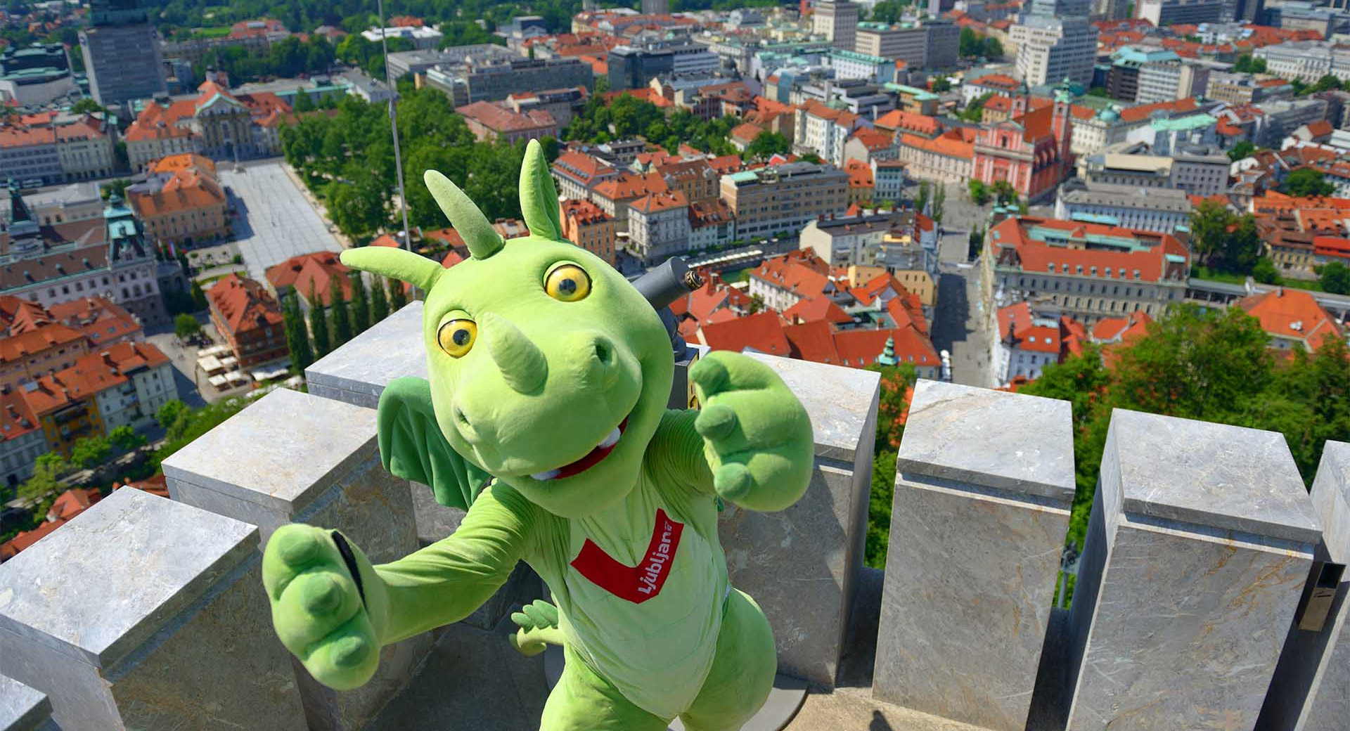 Maskota Ljubljanski zmajček na stolpu Ljubljanskega gradu, pod njim Ljubljana