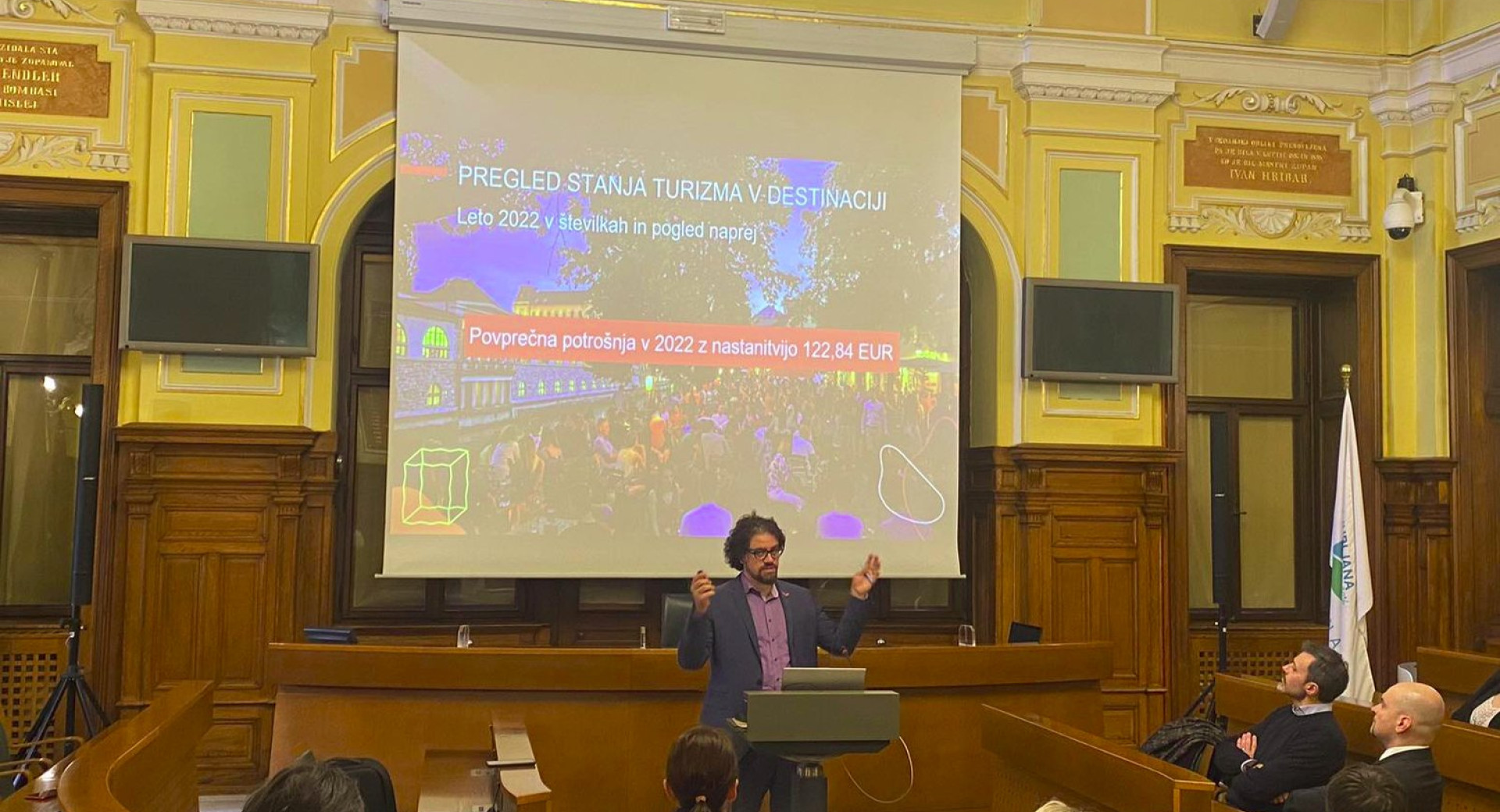Moski nagovarja obiskovalce v dvorani. Na panoju napis Pregled stanja turizma v destinaciji.