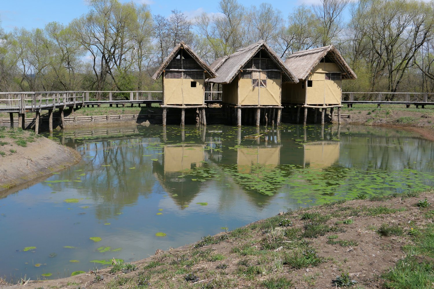 Tri hiške na kolih ob robu manjšega jezera – poustvaritev bivališč koliščarjev v Hiši narave in koliščarjev – Morostig na Igu