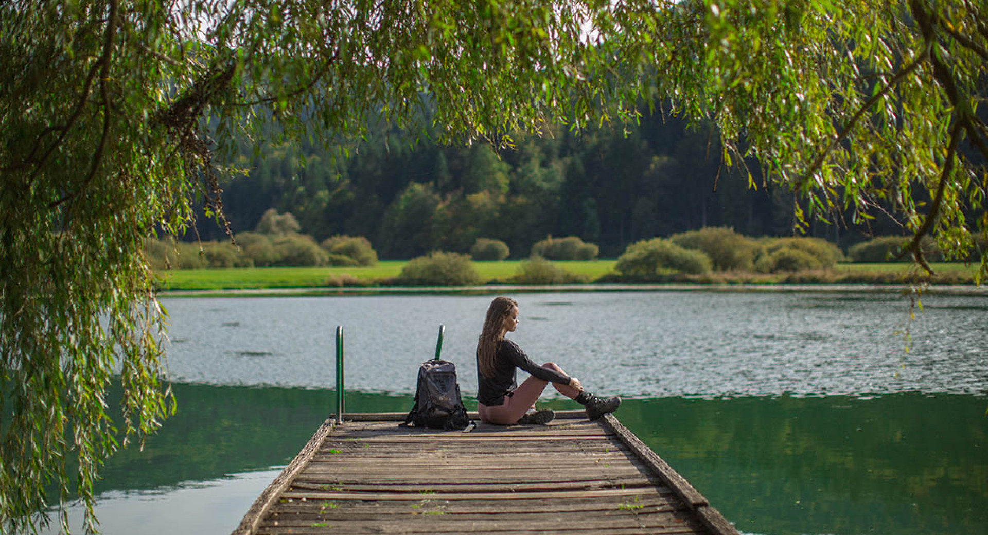 Pohodnica sedi na lesenem podestu nad Podpeškim jezerom ob Ljubljanskem barju