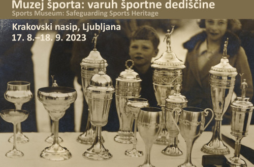 Na crnobeli fotografiji so na mizi pokali. V ozadju otrok in zenska. Gre za napoved razstave Muzej sporta: varuh sportne dediscine.