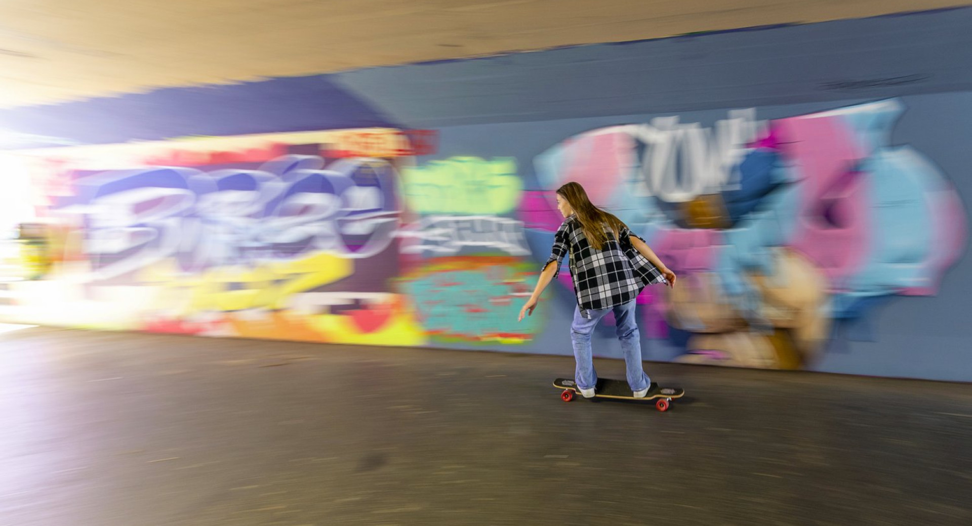 Dekle na rolki ob velikem grafitu v podhodu.