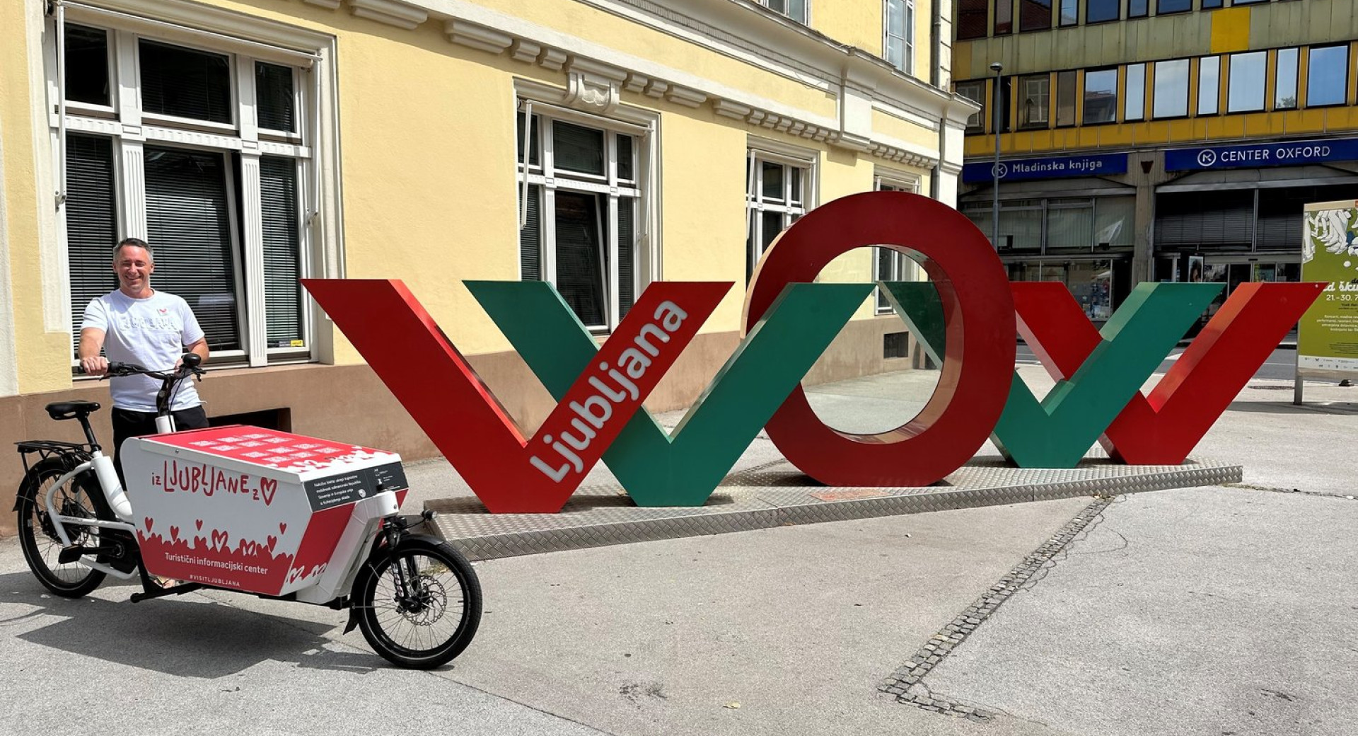 Tovorno kolo, spremenjeno v mobilni turistični informacijski center Turizma Ljubljana, ob njem moški, ki drži krmilo kolesa, zraven je velik WOW znak z napisom Ljubljana na enem od krakov črke w