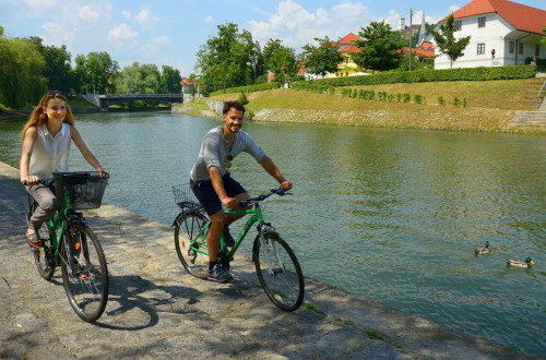 Ženska in moški kolesarita po nabrežju Ljubljanice