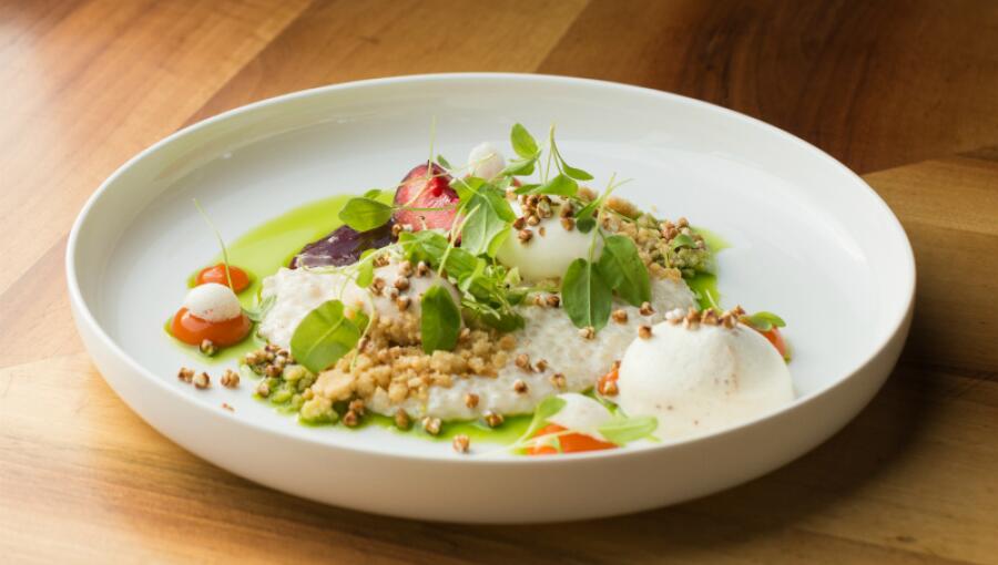 A gourmet dish on a white plate made with a creamy base, buckwheat groats, and colorful fruit.