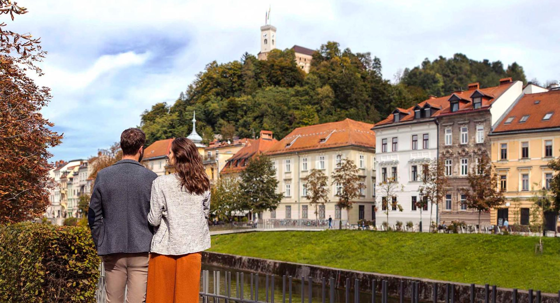 Par stoji na nabrežju Ljubljanice in opazuje staro jedro z Ljubljanskim gradom