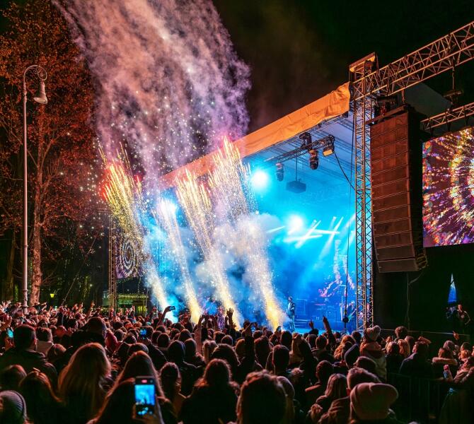 An outdoor concert with fireworks and a lively crowd enjoying the show at night.