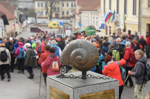 Skulptura polževe hišice pred množico ljudi.