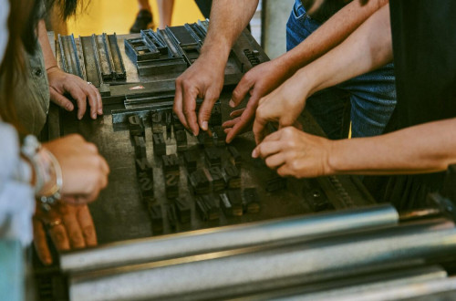 Visitors rearrange the letters on a printing press.