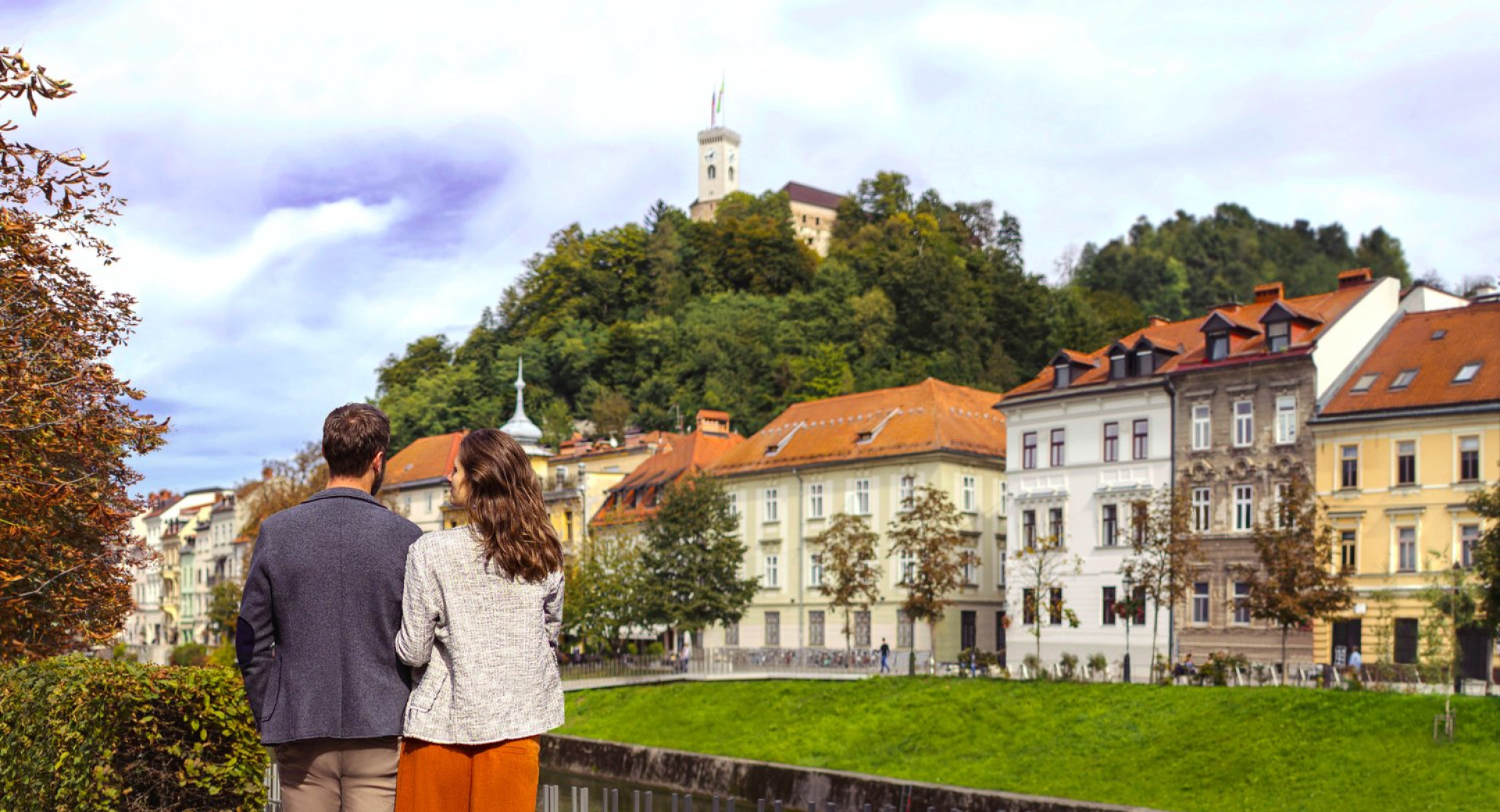 Par stoji ob Ljubljanici in zre proti Ljubljanskemu gradu