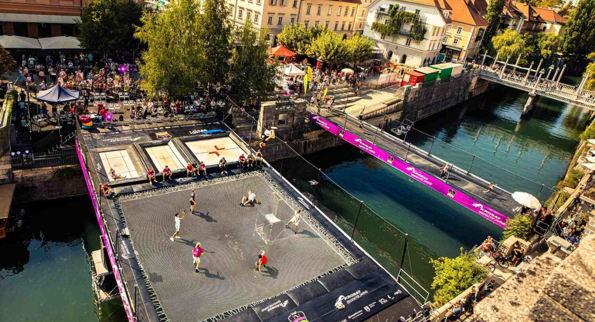 Utrinek z dogodka WOOP! Odbito na Ljubljanici/Made by Akrobat; na Ljubljanici sta velik trampolin in trampolinski most, na nabrežju gledalci, 2022