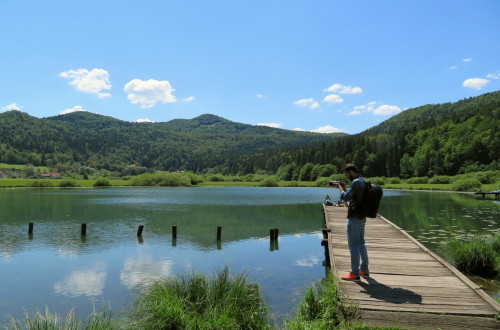 Jezero in fotograf na lesenem pomolu. V ozadju hribi.