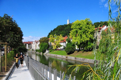 Sprehajalci ob Ljubljanici. V ozadju je Ljubljanski grad.