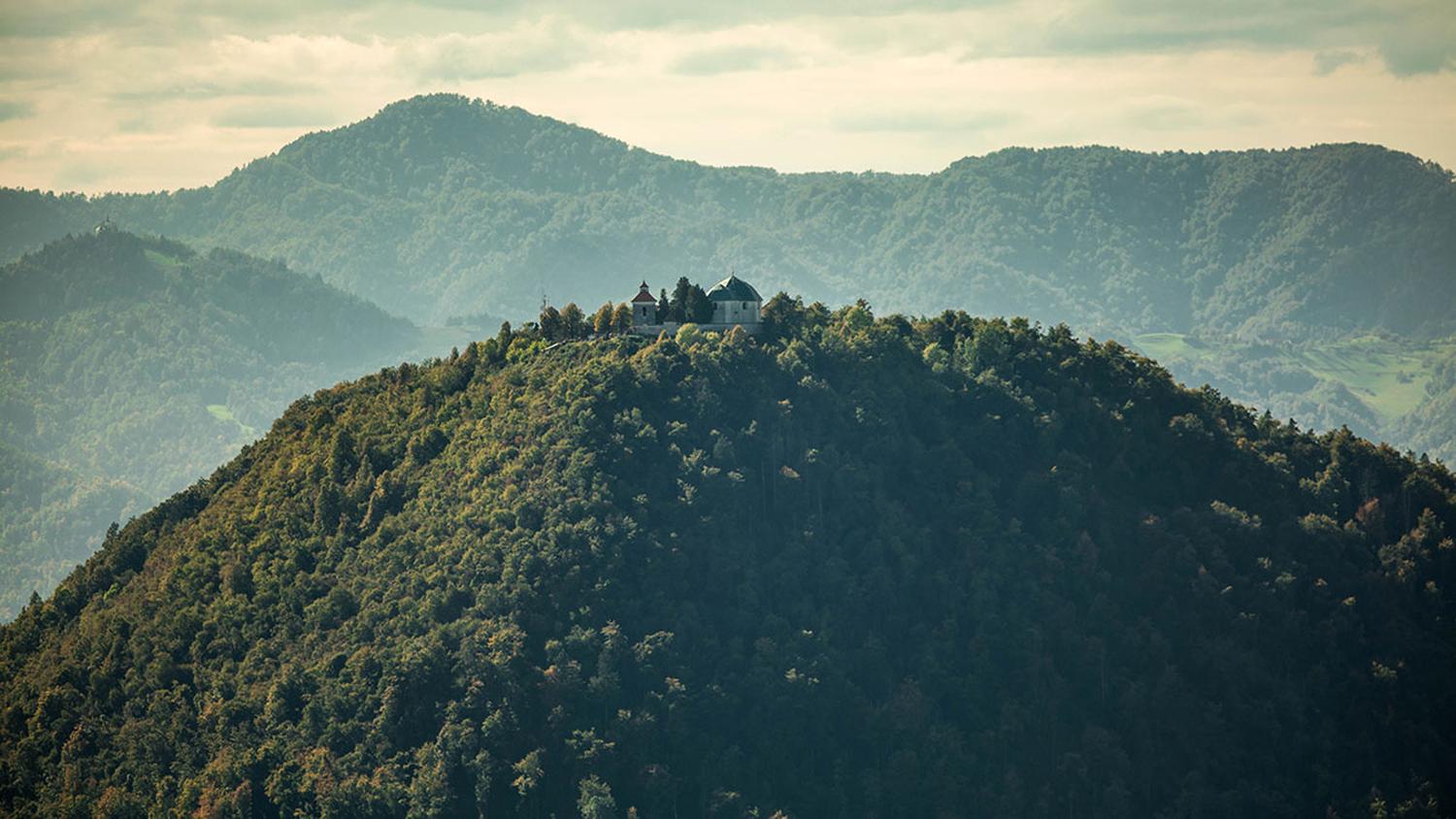 Panoramska slika gore s cerkvico na vrhu.