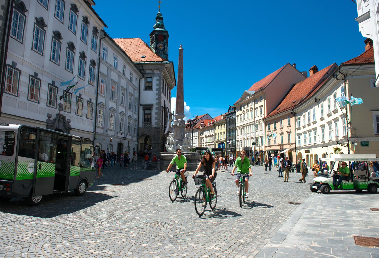 Trije kolesarji na mestnem trgu v Ljubljani.