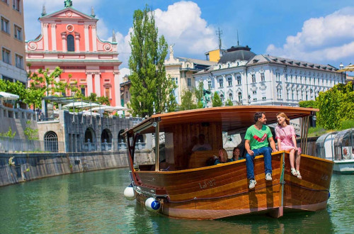 Par sedi na ladjici po Ljubljanici. V ozadju cerkev sv. Frančiška.