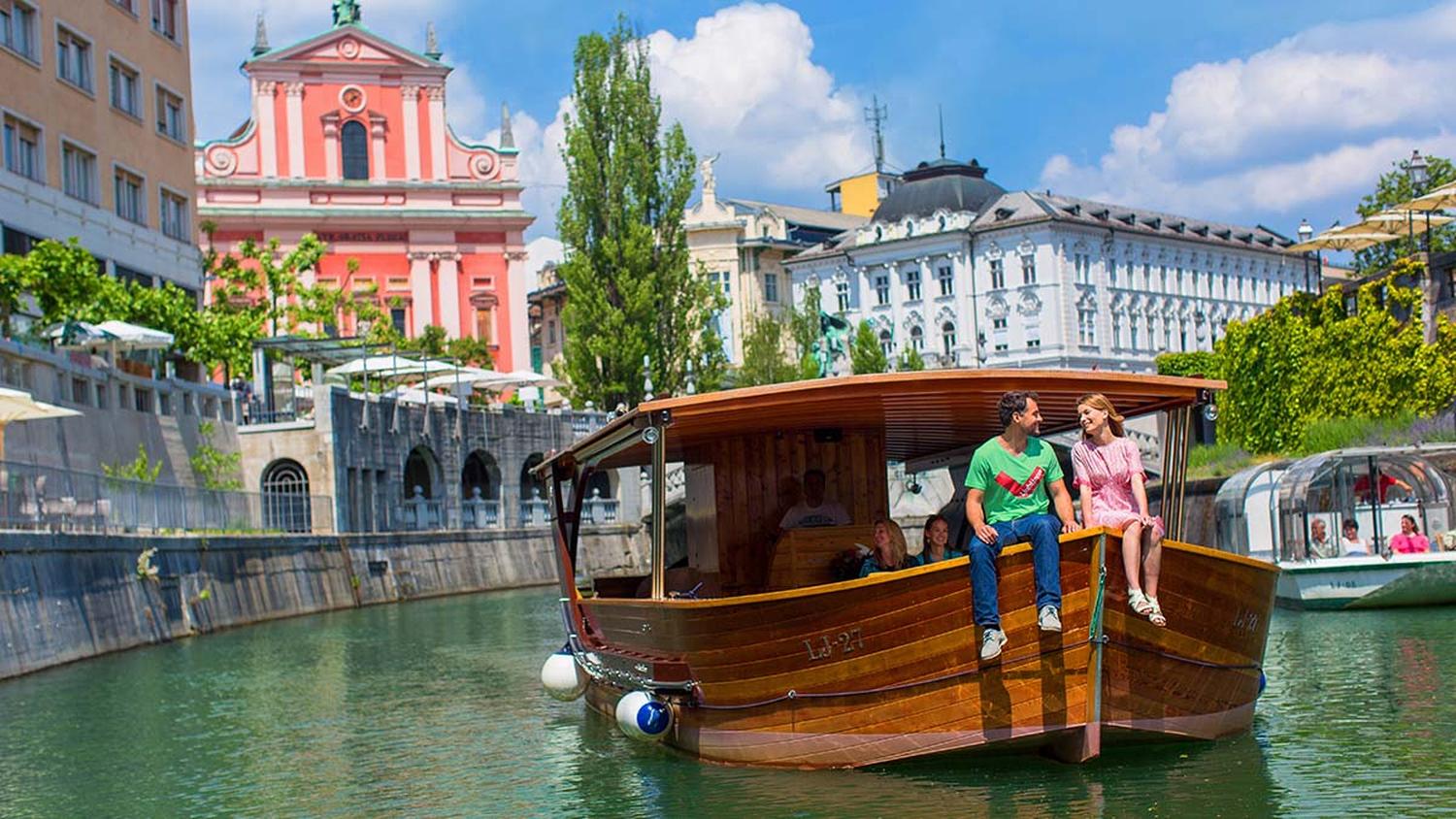 Par sedi na ladjici po Ljubljanici. V ozadju cerkev sv. Frančiška.