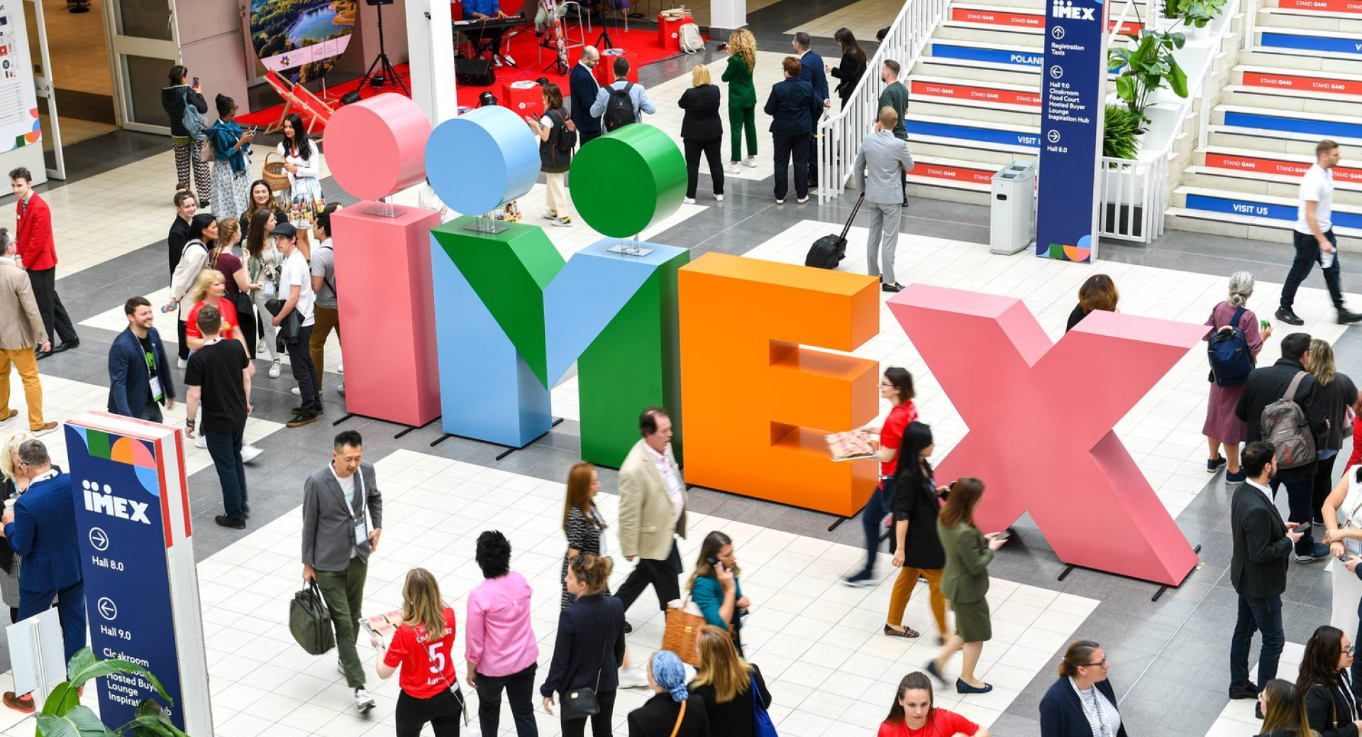 Obiskovalci na mednarodni borzi industrije srečanj IMEX v Frankfurtu, maj 2023; v sredini je postavljen velik napis iz črk različnih barv – IMEX