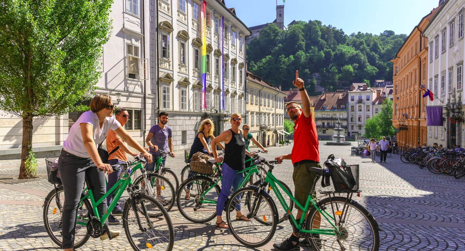 Skupina turistov na kolesu z vodnikom v Ljubljani; v ozadju Novi trg in Ljubljanski grad