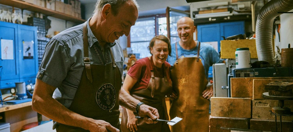Obiskovalca opazujeta mojstra med prikazom rocne izdelave srebrnega nakita.