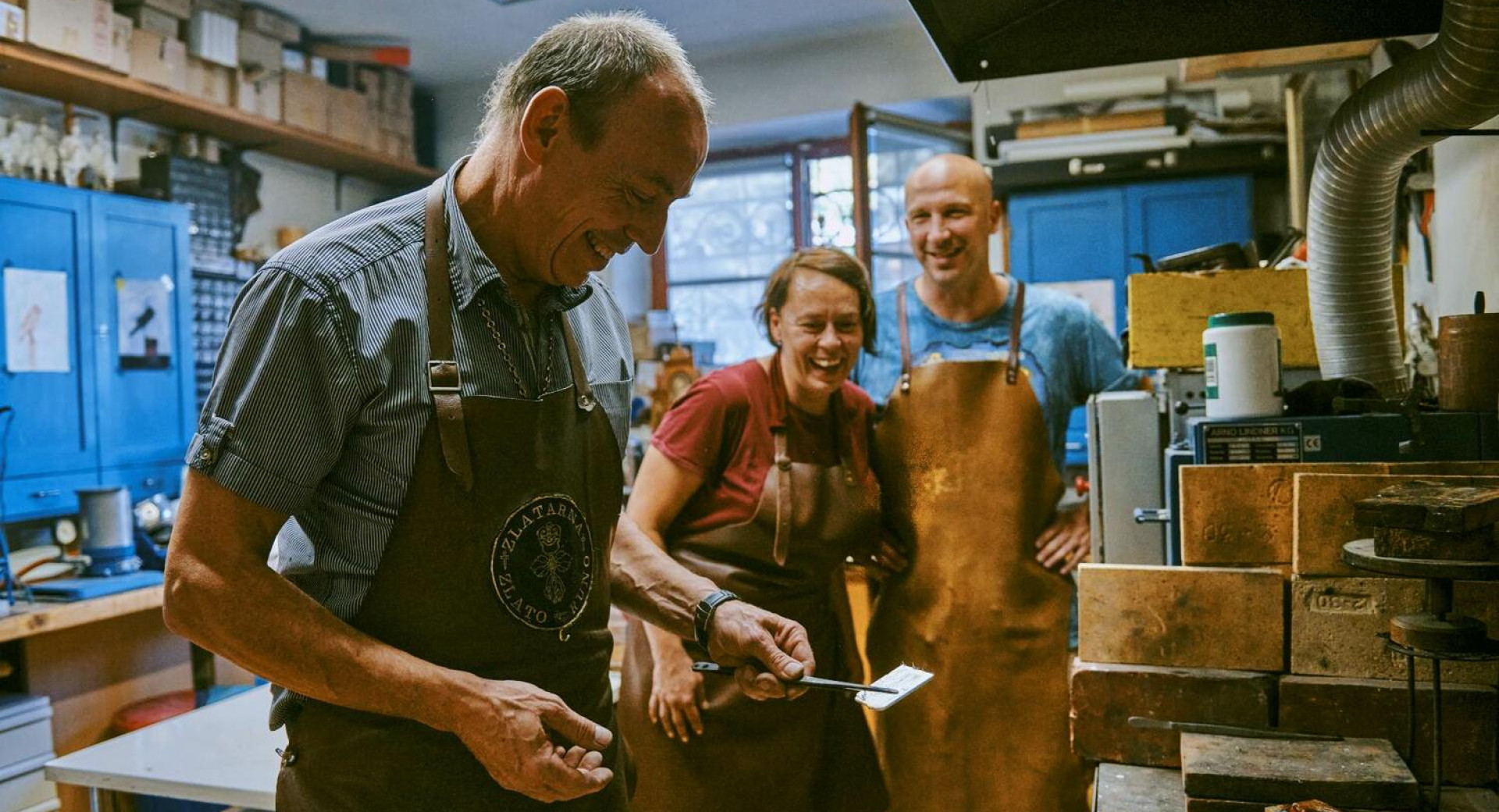 Obiskovalca opazujeta mojstra med prikazom rocne izdelave srebrnega nakita.
