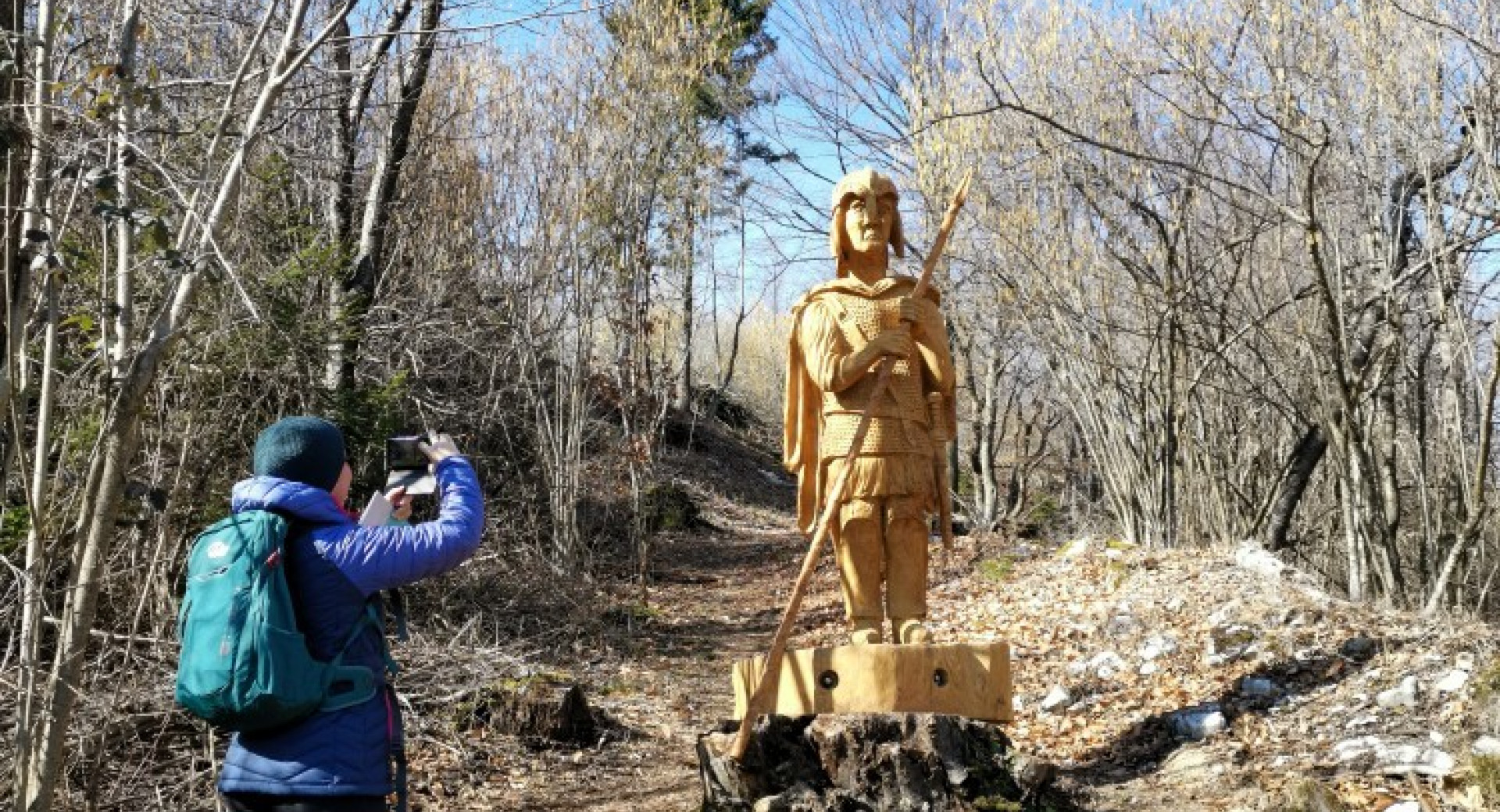 Obiskovalec fotografira lesen kip vojaka. 