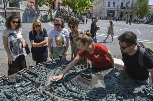 Turistična vodnica s skupino obiskovalcev pred maketo Ljubljane na Prešernovem trgu