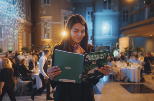 Zenska stoji. V rokah drzi revijo Gourmet Ljubljana.