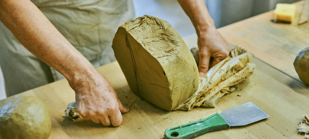 Velik kos gline na mizi. Zenska reze glino.