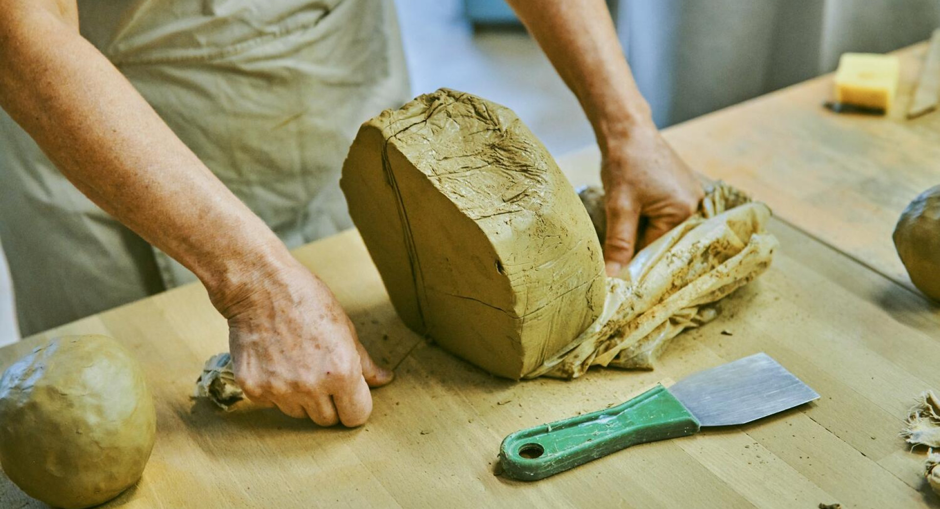 Velik kos gline na mizi. Zenska reze glino.