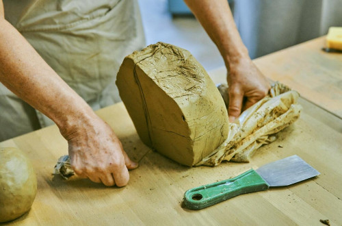Velik kos gline na mizi. Zenska reze glino.