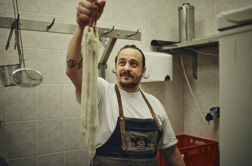 Moski s predpasnikom drzi v roki vrvico z nekaksno podolgovato klobaso.