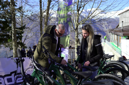 A man and a woman are leaning over green mountain bikes. Mountain bikes set in a natural environment.