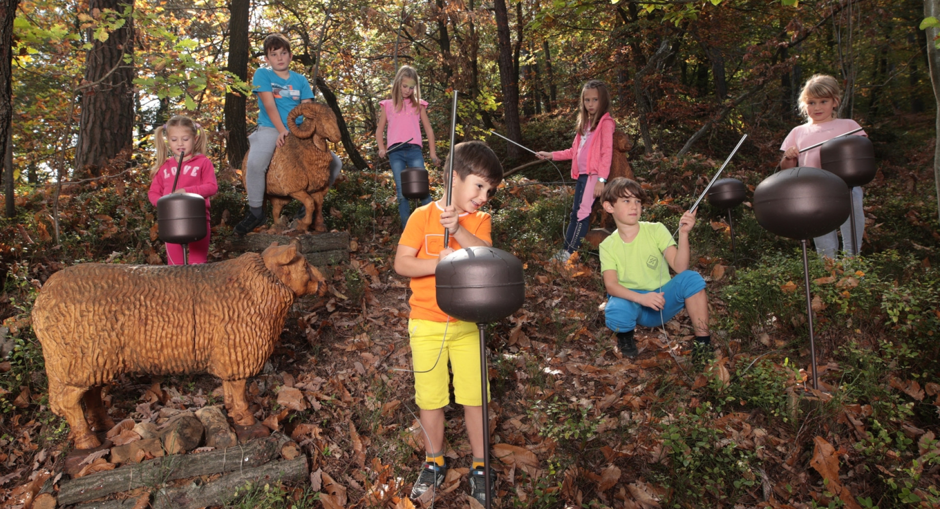 Skupina otrok na prvi zvočni planinski poti v Sloveniji Zven zaklete grofice v gozdu na Dobrovi na točki z glasbili in dvema lesenima skulpturama živali