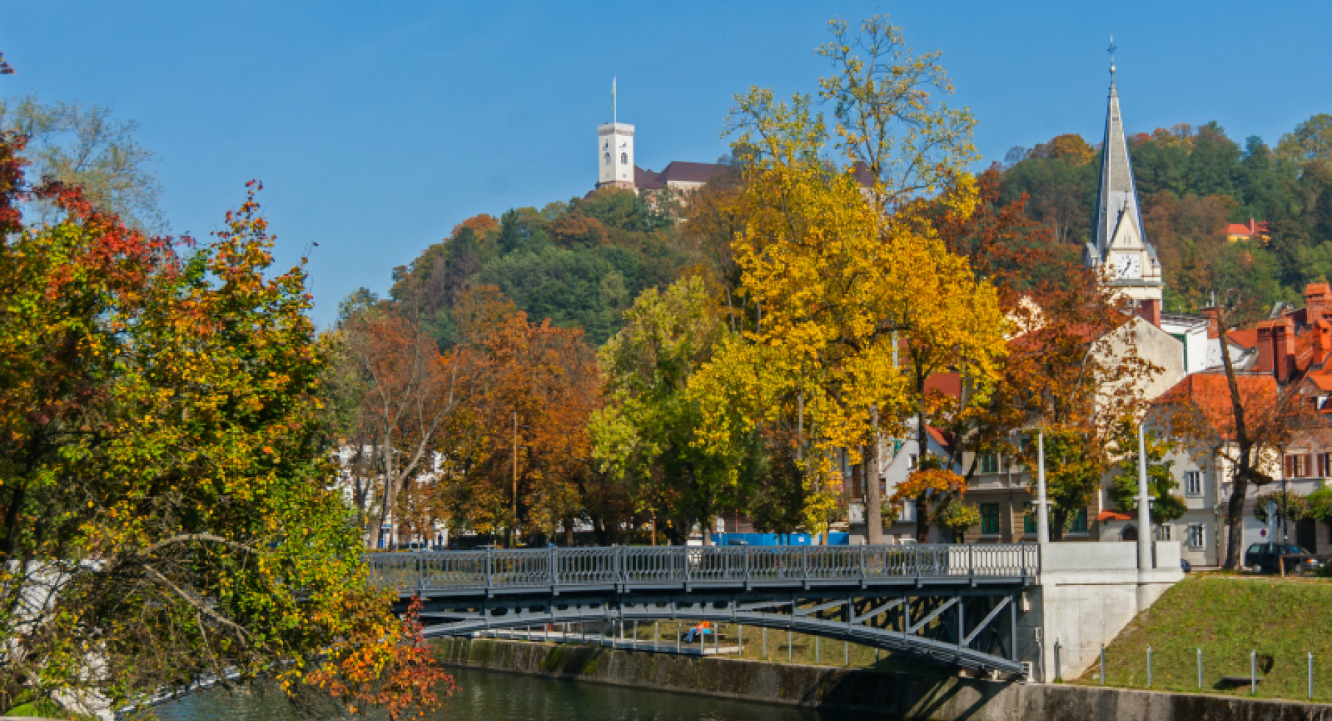 Ljubljanica jeseni. V ozadju most, cerkev in Ljubljanski grad.