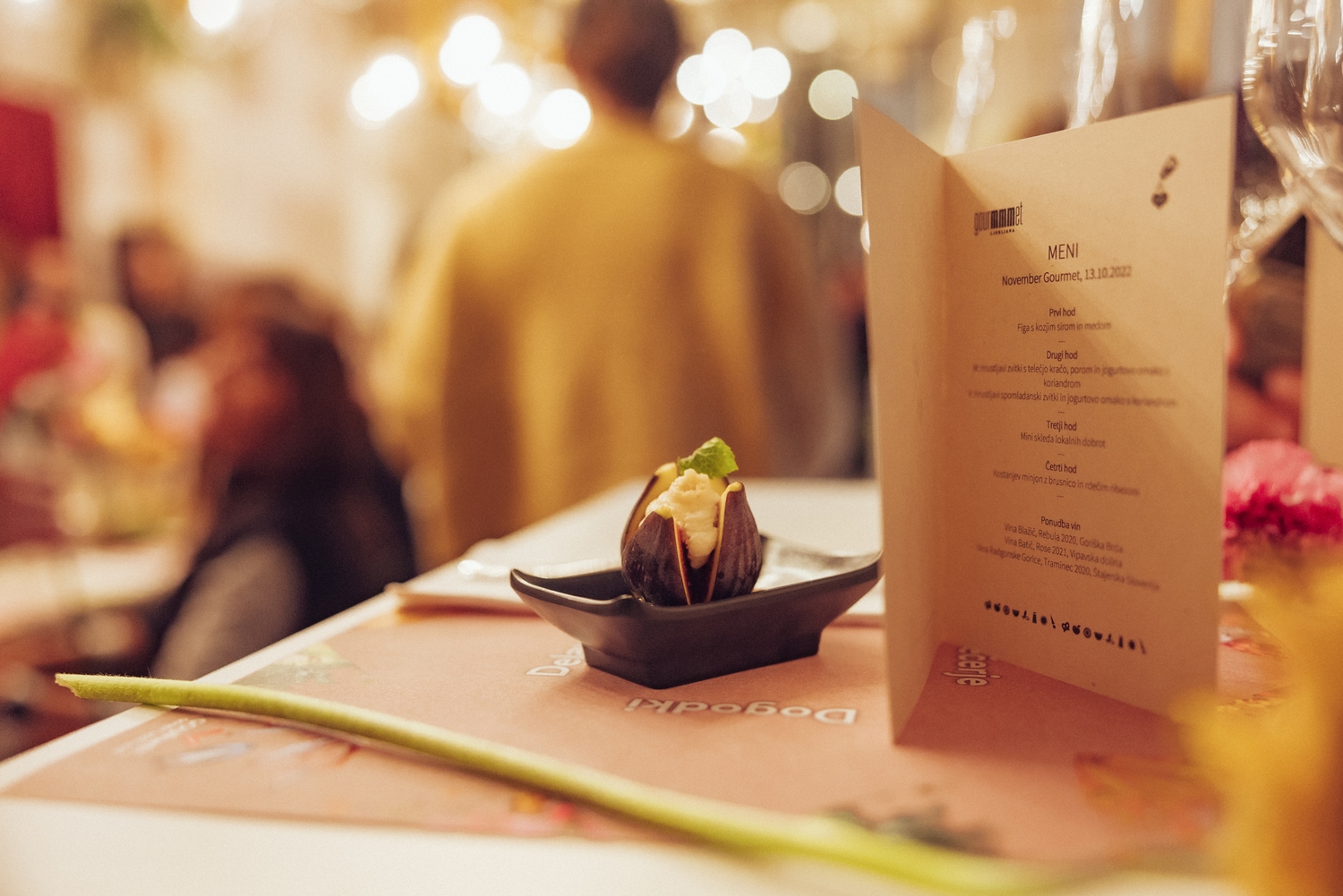 Na mizi odprt jedilnik in ob njem sladica na majhne krožniku; napoved festivala November Gourmet Ljubljana 2022