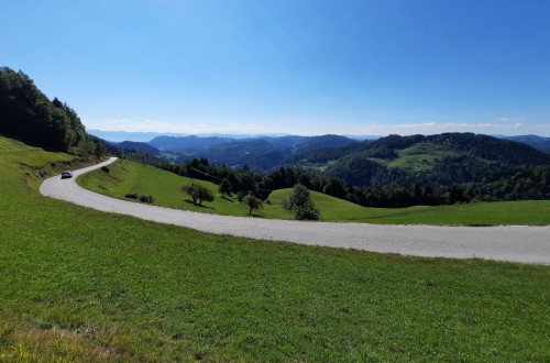 Polhograjski Dolomiti - zeleni travniki, ki jih reže cesta, in gozdovi, v ozadju hribi