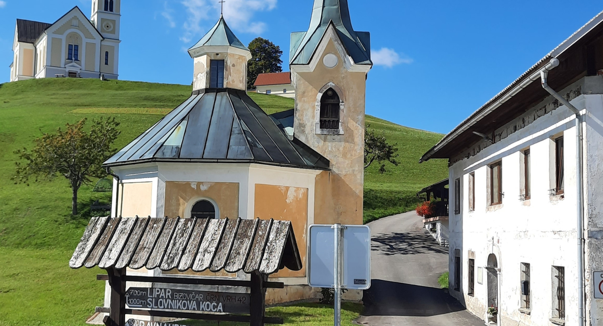 Cerkev sv. Lenarta, osrednja veduta Črnega Vrha v Polhograjskem hribovju, v ospredju kapelica