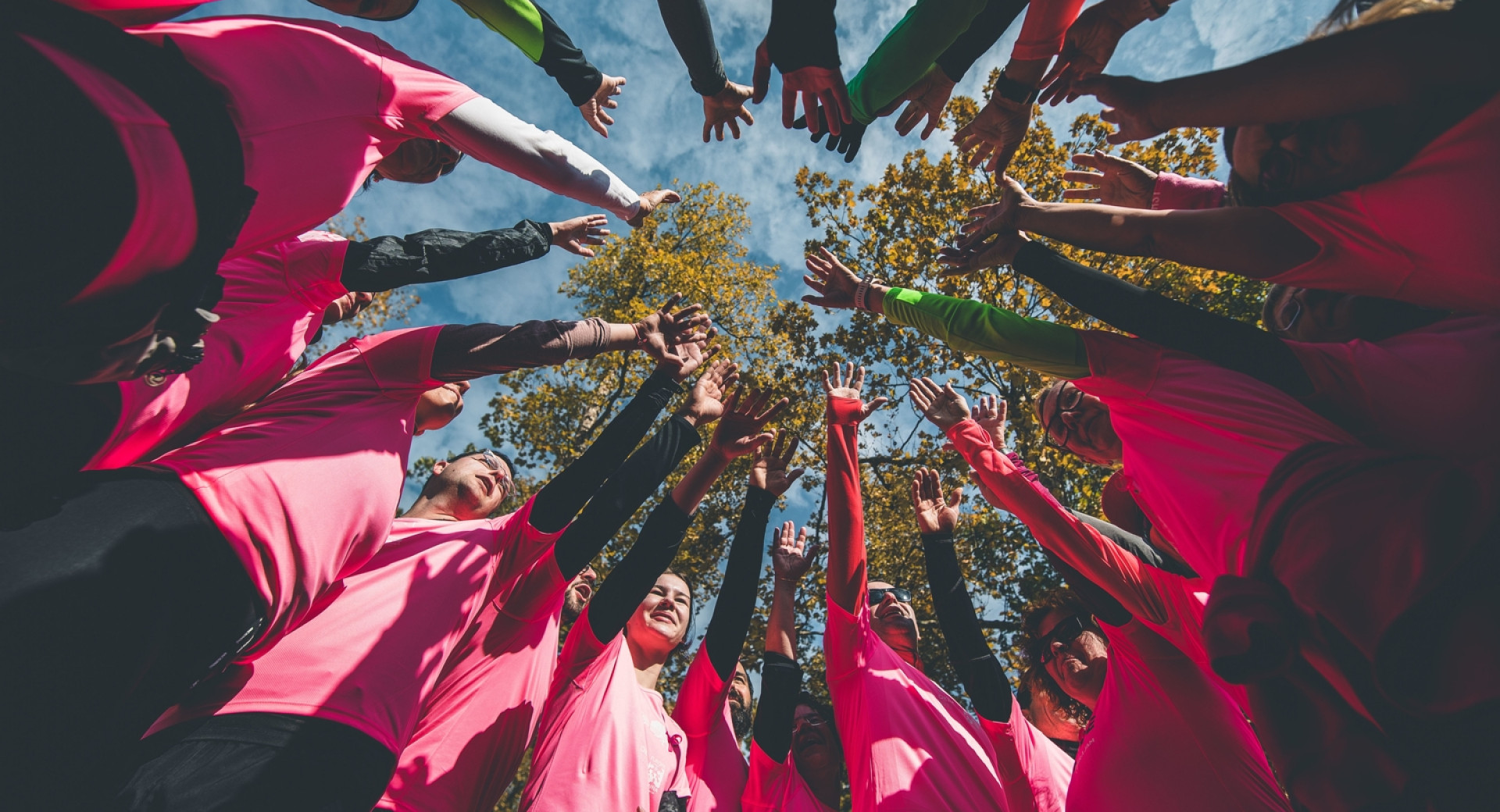 Skupina ljudi v rožnatih majicah stoji v krogu in drži roke kvišku v skupni pozdrav; Rožnati maraton v Ljubljani, 2021
