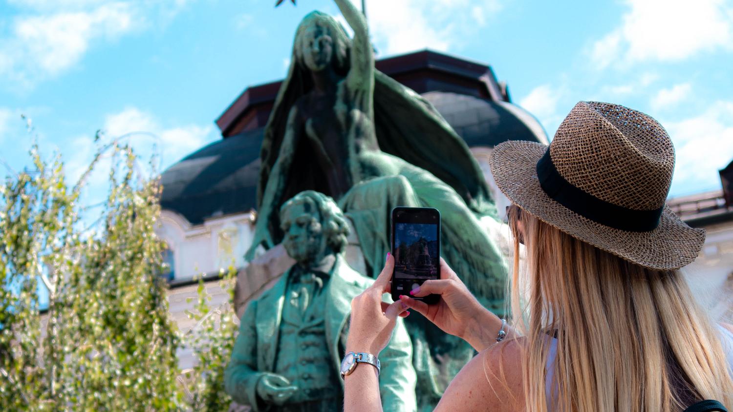 Ženska stoji s telefonom pred Prešernovim spomenikom v Ljubljani