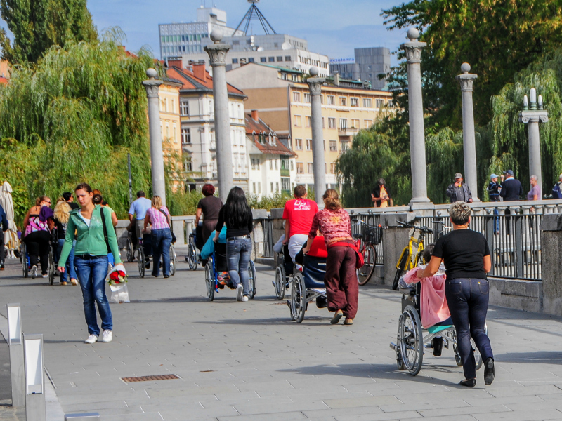 Ljudje, večinoma na invalidskih vozičkih s spremljevalci, na Čevljarskem mostu v Ljubljani