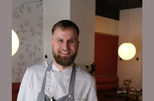 nasmejan kuhar v restavraciji, v beli majici in sivem predpasniku