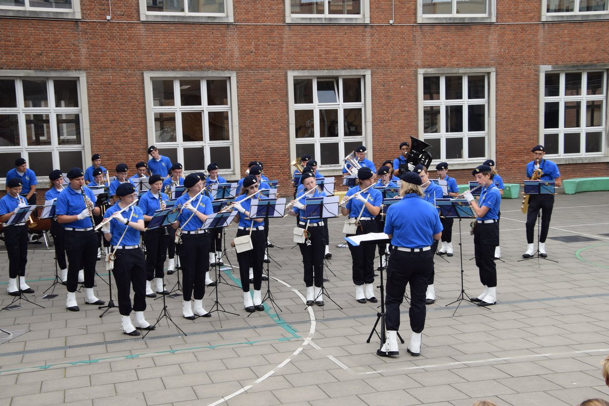 orkester v modrih uniformah igra pred stavbo