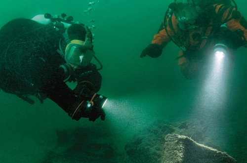 Two divers are exploring the deep water with handheld torches.