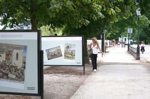 On the street, beneath the trees, there are display panels featuring old postcards by Maksim Gaspari.