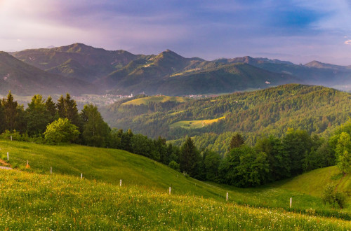 Pogled z vrha na zelene hribe in vas v daljavi.