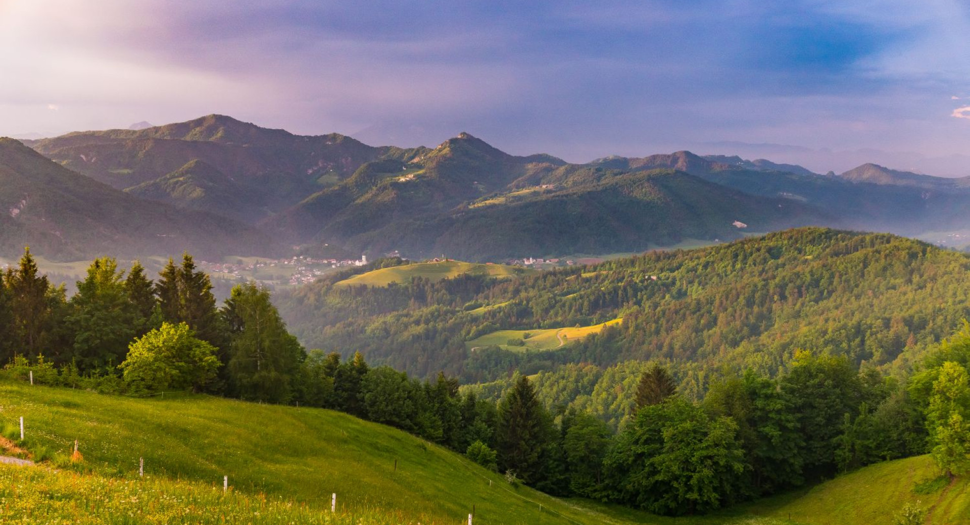 Pogled z vrha na zelene hribe in vas v daljavi.